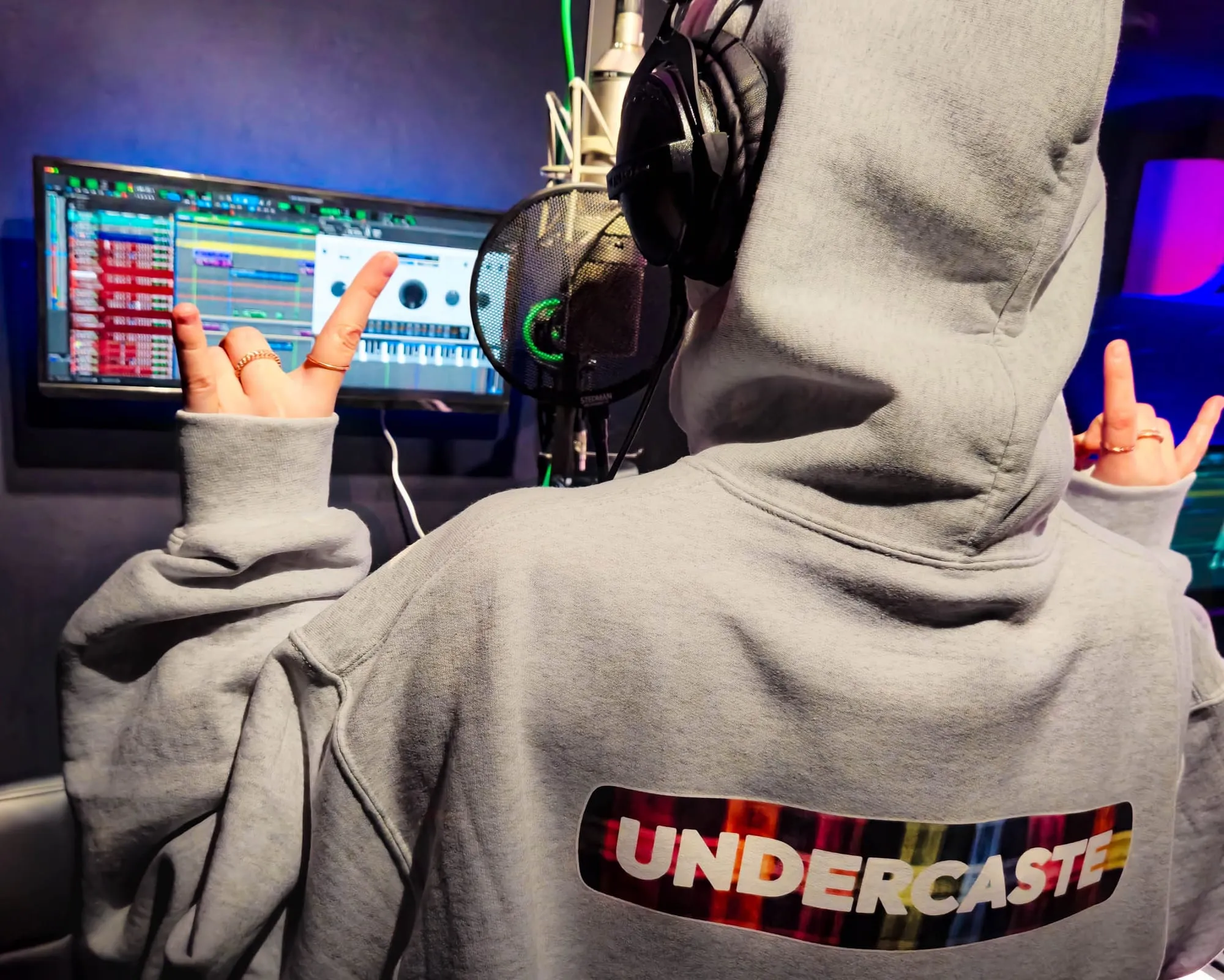 An artist in an Undercaste hoodie at the booth glass, session on screen.