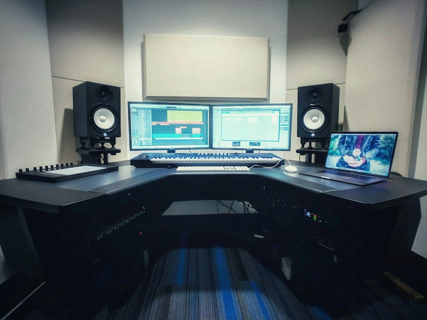 A dark self-serve studio desk with dual monitors and speakers.