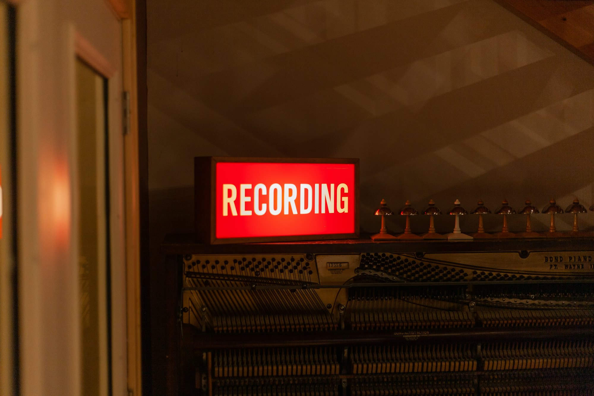 A red neon "RECORDING" sign glowing in a dark studio hallway.